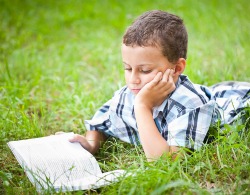 Cute kid reading a book while lying in grass